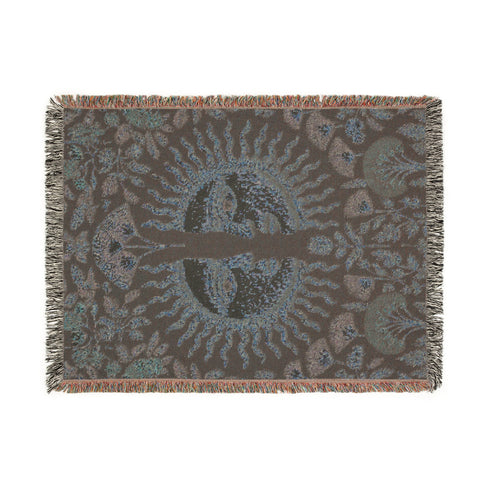 Jacquard-woven cotton blanket featuring twin celestial suns—two serene faces meeting at center—with radiant golden rays on a charcoal ground, bordered by folkloric botanicals and fan blossoms in sage, sky, and garnet. Crafted from 100% soft cotton yarn; the artwork is woven, not printed. Reversible with a color-negative back and finished with a protective 2-inch multicolor fringe. Sizes: 52×37, 50×60, 60×80 for wall, sofa, or queen-bed layering.
